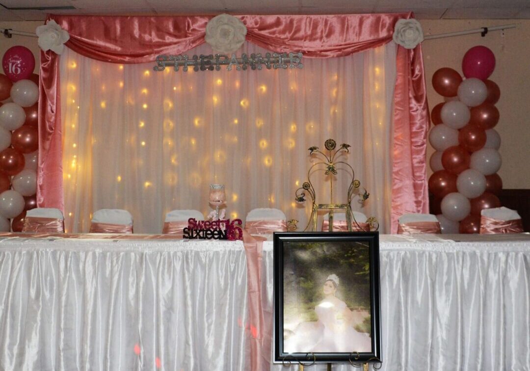 A room with a table and chairs, lights, balloons and a picture.