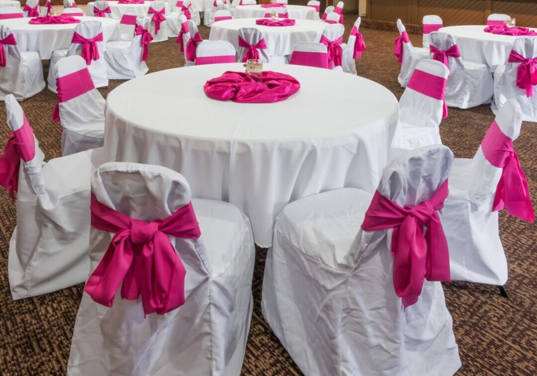 A room with many tables and chairs covered in white cloth.